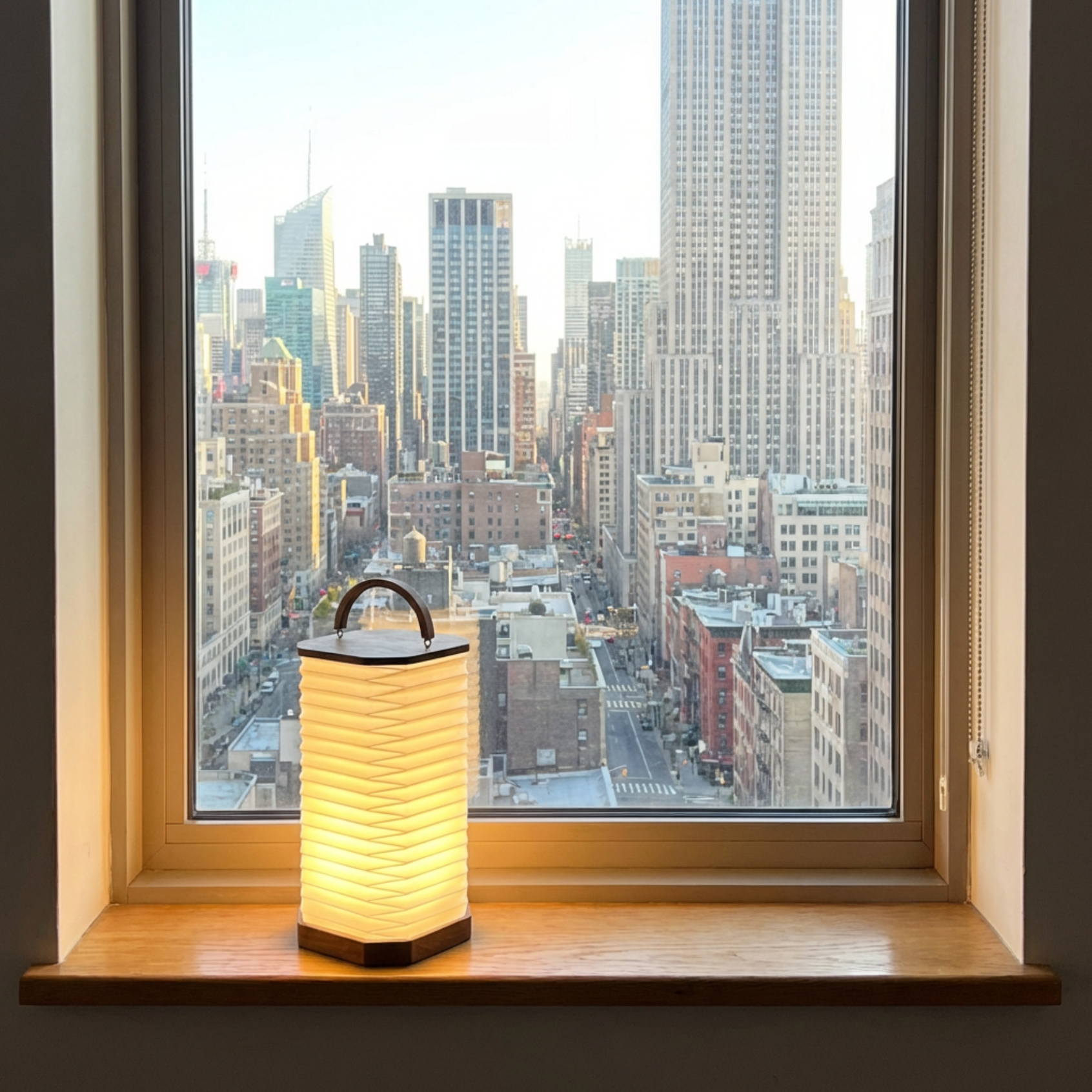 Armonica Table Lamp with a warm glow, placed on a windowsill overlooking a city skyline.