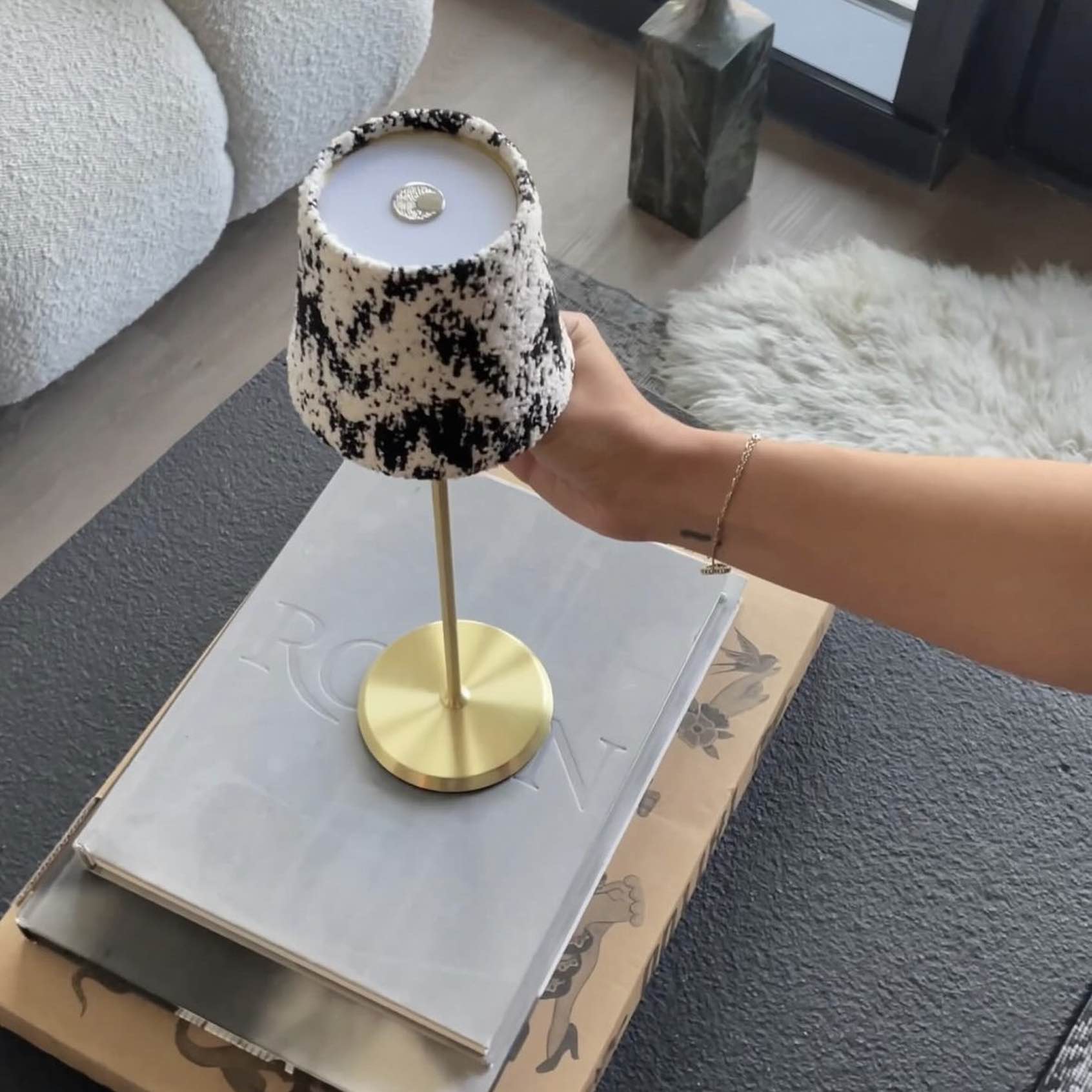 Selene Table Lamp with a black and white patterned shade and a gold brushed base, placed on a stack of magazines.